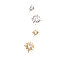 Four small stud earrings displayed on a brown textured card. Two earrings are gold-toned sunburst shapes with clear heart-shaped stones, and two are silver-toned sunburst shapes with clear heart-shaped stones.