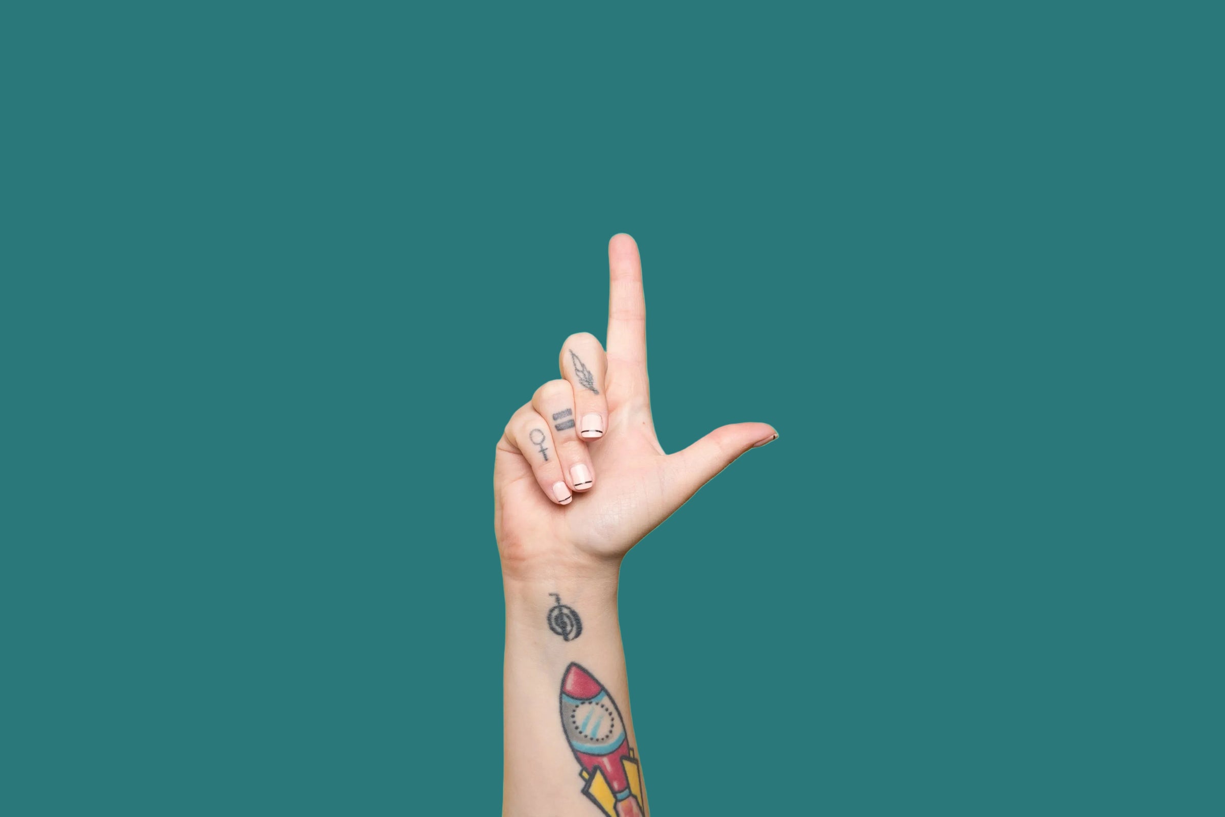 A close-up of a person's hand and wrist making a peace sign, featuring various colorful tattoos including a small rocket ship, set against a solid bright cyan background.
